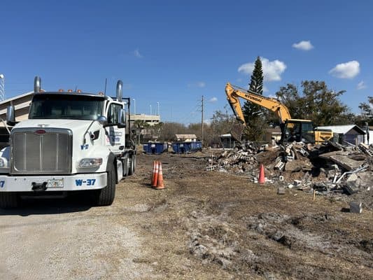 South Vue excavator mid-teardown beside a loaded haul truck and demolition debris on a Tampa job site
